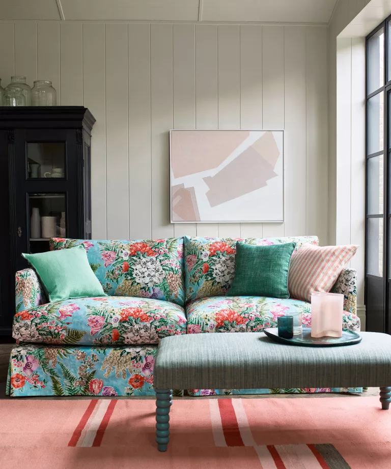 Salon avec canapé bleu à fleurs, tapis rose, armoire noire et œuvres d'art.