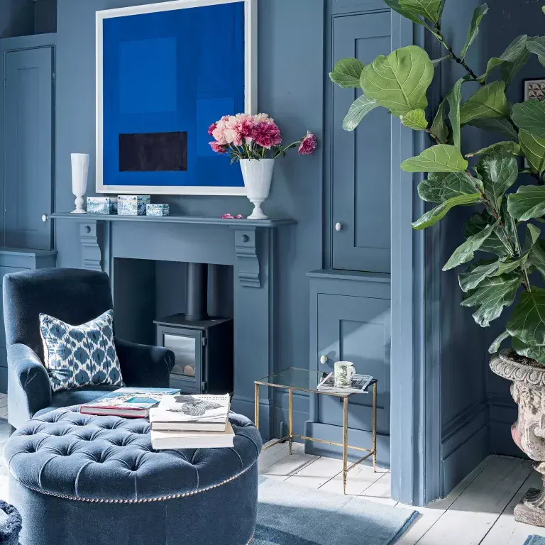 salon bleu avec œuvre d'art au-dessus de la cheminée, fauteuil et ottoman