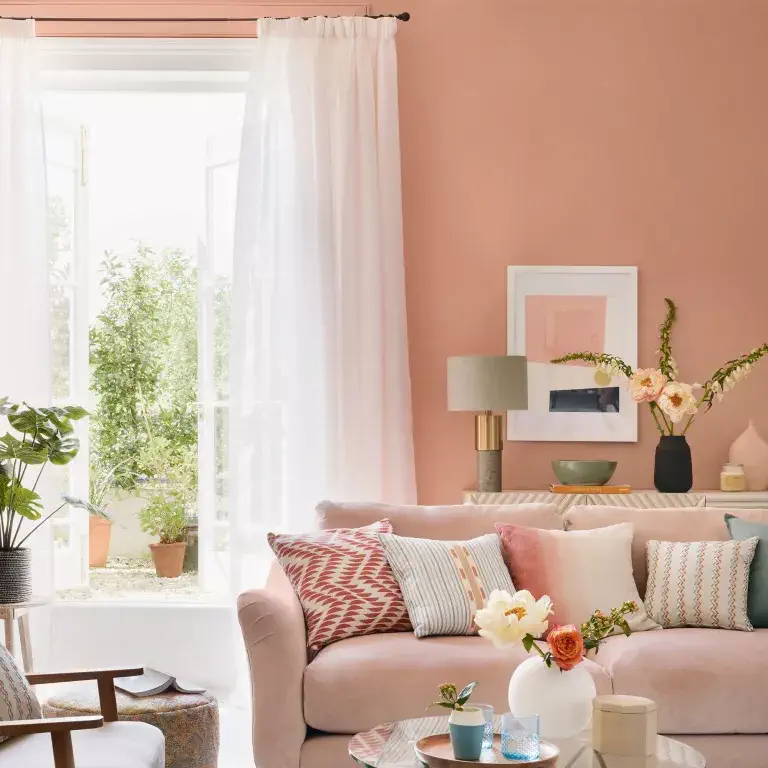 Salon rose avec canapé, table d'appoint et rideaux blancs
