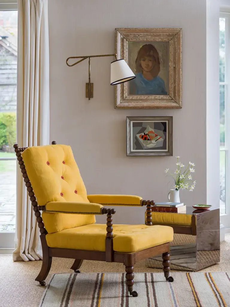salon avec fauteuil jaune, tableaux au mur, table d'appoint et applique murale