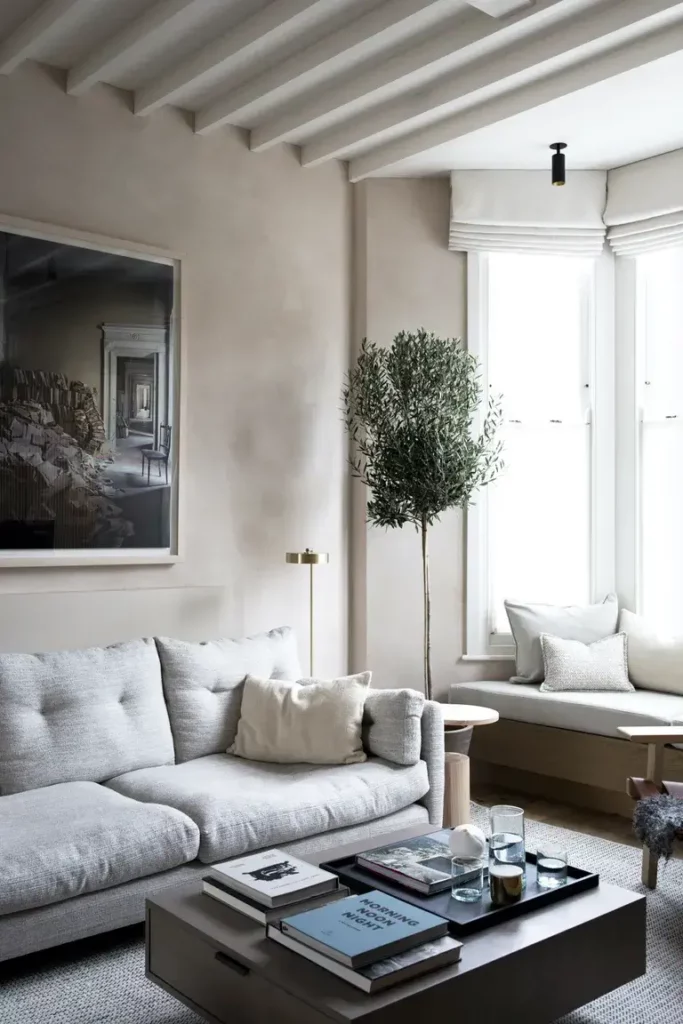 salon neutre avec fenêtre, œuvre d'art, arbre, canapé gris clair, table basse, lampadaire en laiton