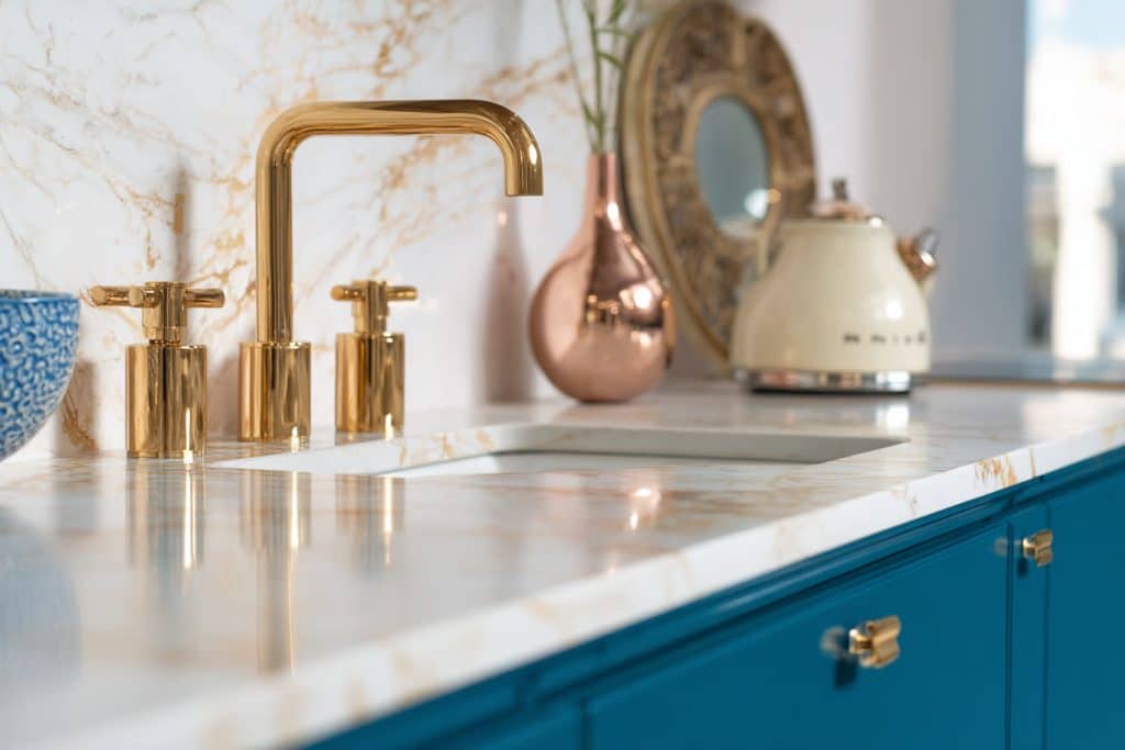 zoom sur le plan de travail blanc marbré doré brillant meubles bleu canard et évier avec robinet doré design chic tendance original