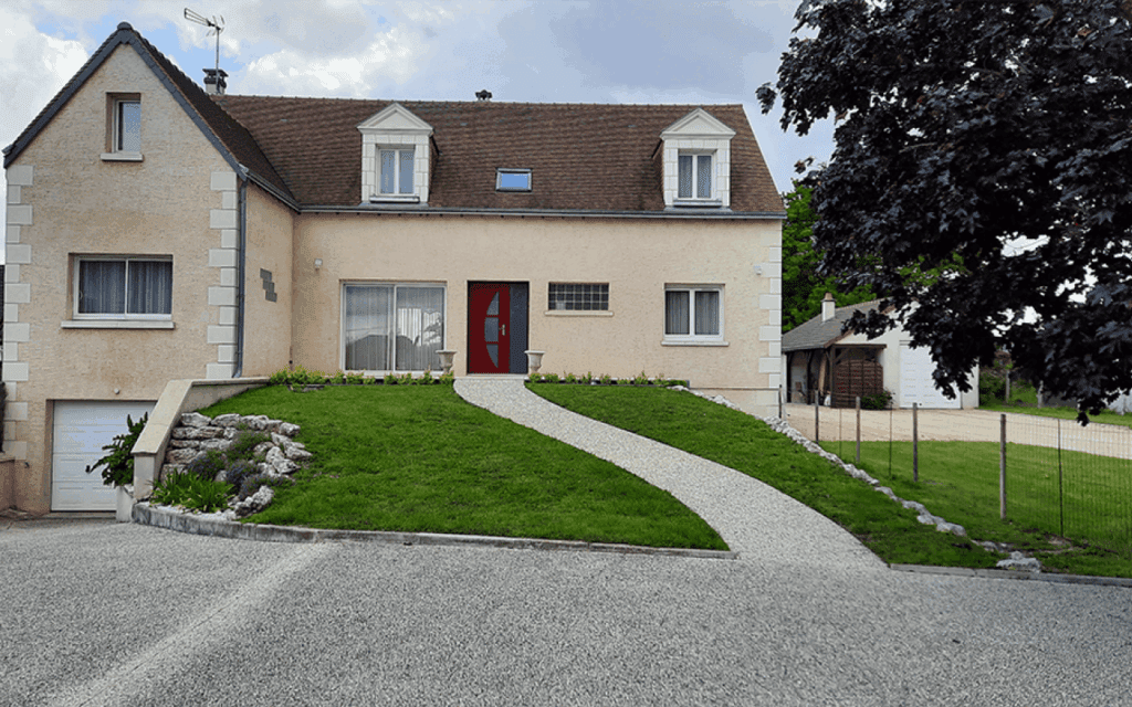 maison construite sur terrain en pente avec garage sur le côté plus bas et belle entrée avec de la verdure